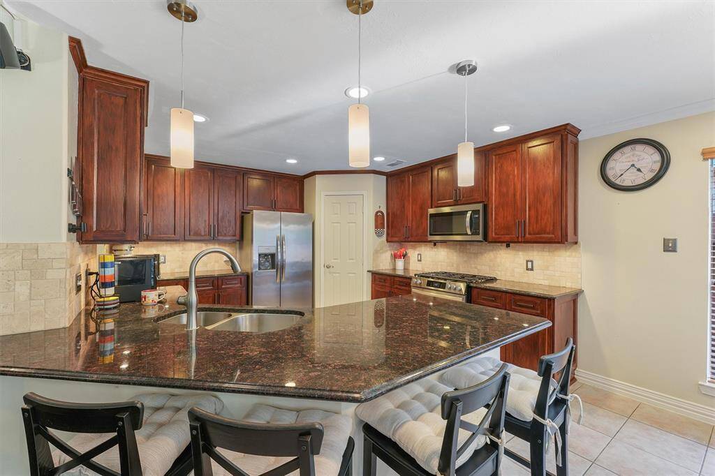 This updated kitchen features rich, dark wood cabinetry, granite countertops, and stainless steel appliances and a breakfast bar.