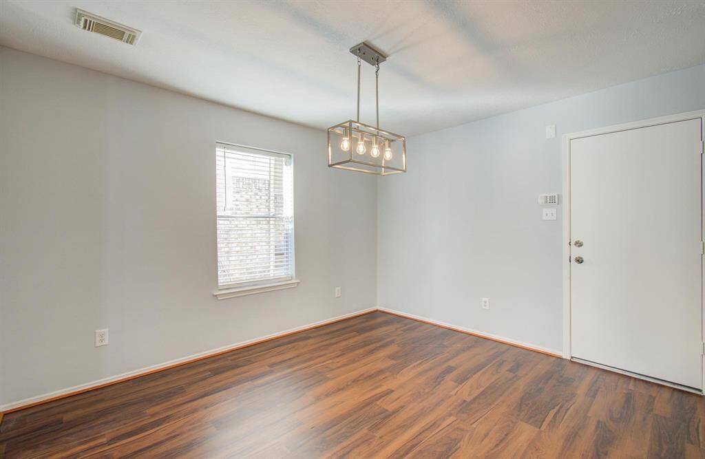 This photo shows a bright dining room with light gray walls and vinyl flooring. It features a window providing natural light and a modern rectangular ceiling light fixture which would be featured over your dining table.