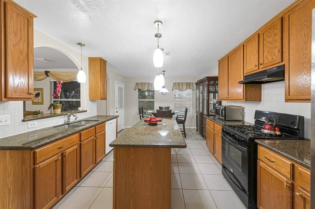 The layout of this space is efficient, witheverything you need within arm'sreach. Take note of the gas range with many burners. Above the range is a complementing range hood, blending seamlessly with the white tile backsplash.
