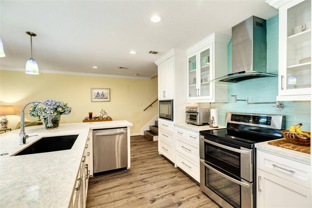 Kitchen backsplash is a beautiful soft blue glass tile. The stove has a double oven, pot filler and stylish vent hood