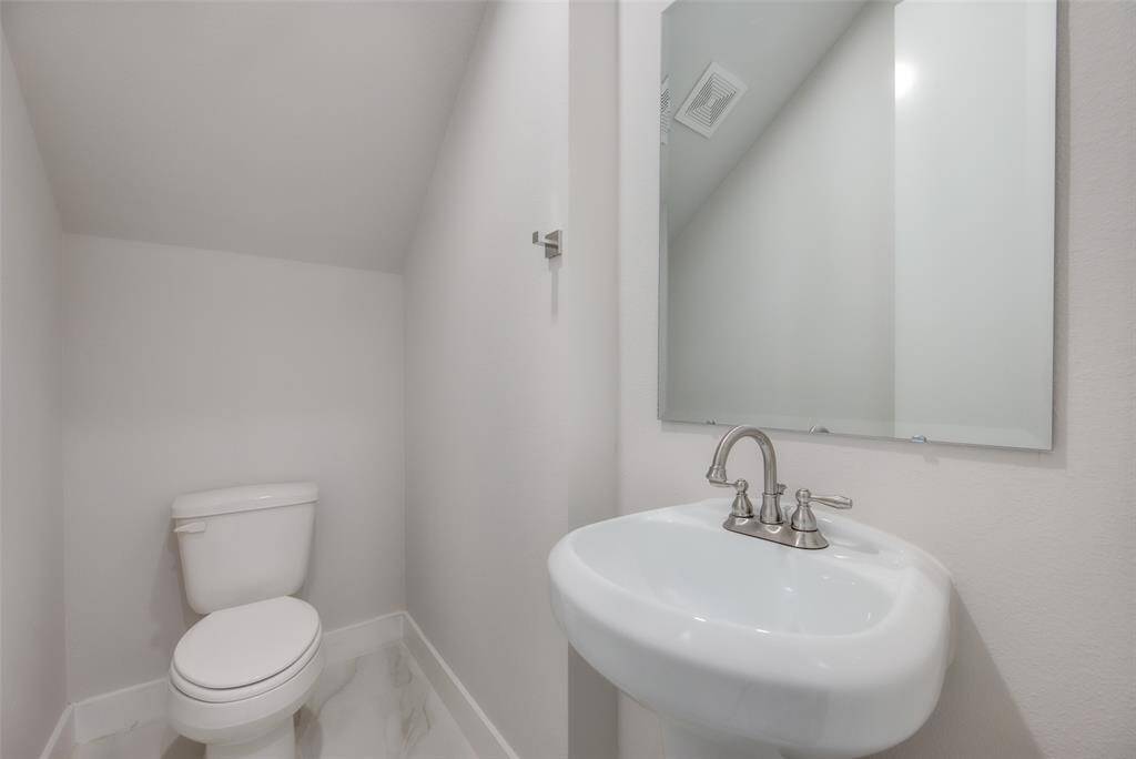 This sleek half bathroom offers a minimalist design with a pedestal sink and modern fixtures. The clean lines and bright lighting create a fresh and inviting atmosphere, perfect for guests and everyday use.