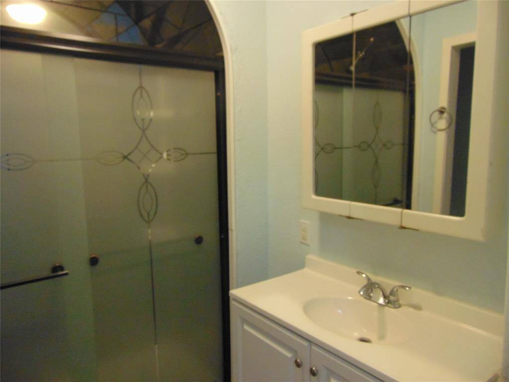 This kitchen features light blue walls, laminate wood flooring, and white cabinets with ample storage. It includes a double sink, an electric stove, a refrigerator, and a ceiling fan, creating a functional and airy cooking space.