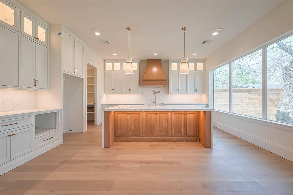 Custom built cabinetry at kitchen complemented by a stunning white oak island with a waterfall edge and matching white oak vent hood for seamless style. Photos as of 03/20/2025.