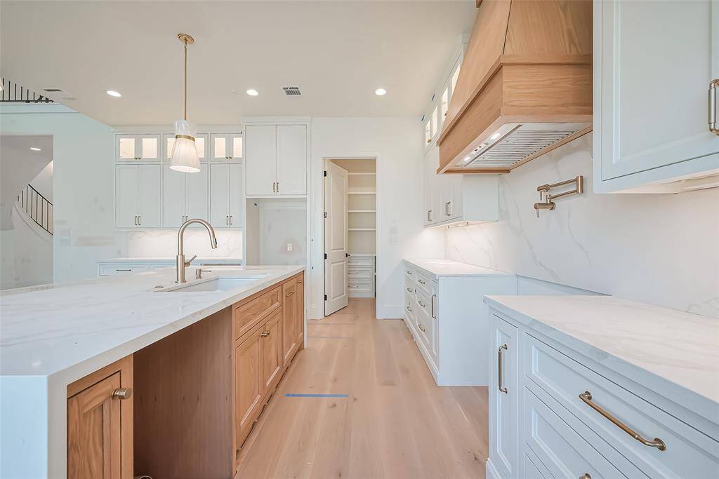 Custom built cabinetry at kitchen complemented by a stunning white oak island with a waterfall edge and matching white oak vent hood for seamless style. Photos as of 03/20/2025.
