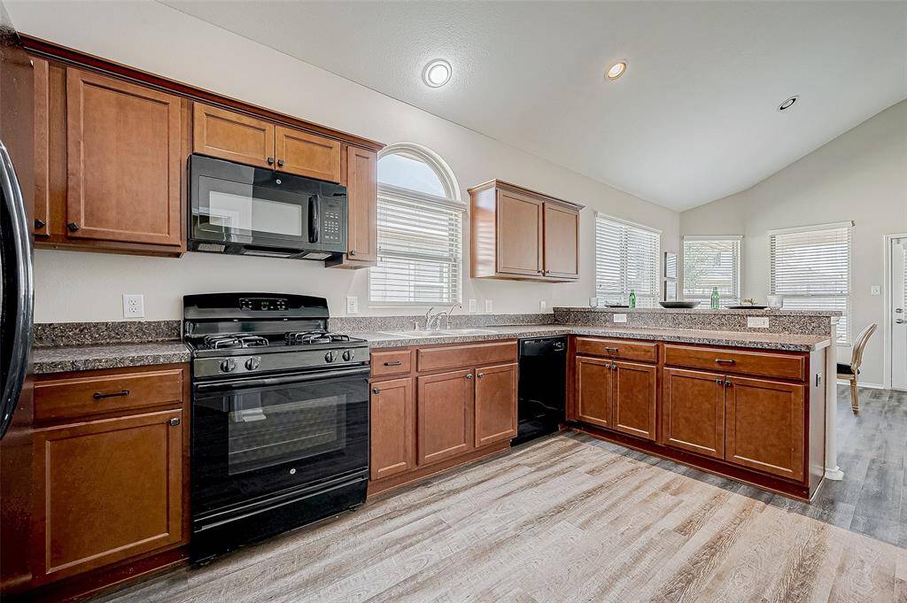 The kitchen is a blend of style and functionality, featuring rich wood cabinetry and sleek black appliances. Granite-look countertops provide ample prep space, while large windows fill the space with natural light. With its open design, this kitchen is perfect for cooking, entertaining, and staying connected with family and guests.