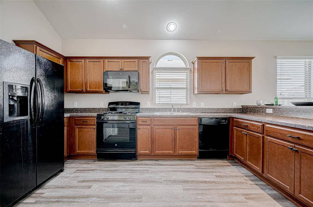 This spacious kitchen features a full suite of sleek black appliances, including a side-by-side refrigerator and gas range. The warm wood cabinetry offers ample storage, complemented by durable countertops and a large window over the sink that lets in natural light. Perfectly designed for both everyday cooking and entertaining, this kitchen is a true centerpiece of the home.