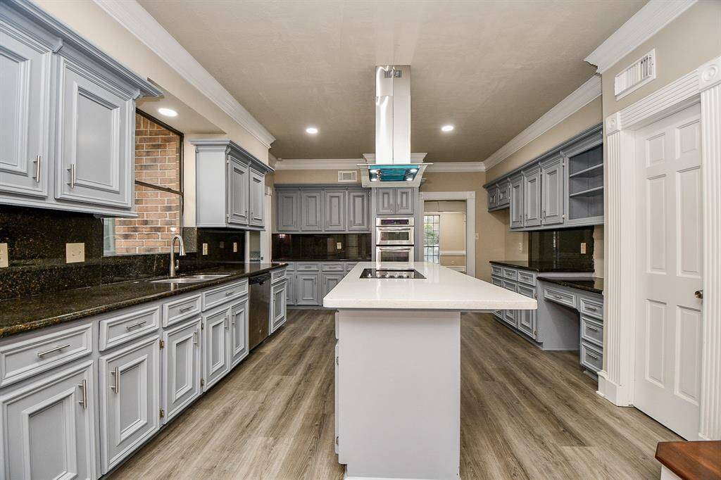 This inviting photo highlights the kitchen's versatility, showcasing built-in bookcases at one end of the island, perfect for displaying cherished cookbooks or decorative items. A glimpse into the shelves above the desk area hints at the abundant storage space available throughout this well-appointed kitchen.