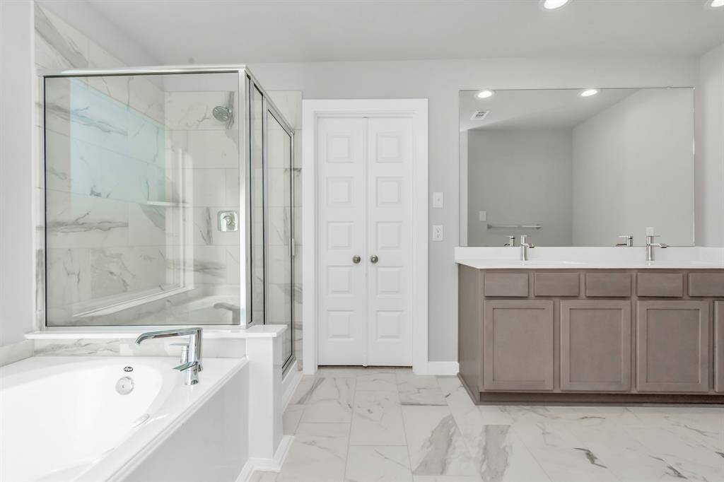 Indulge in a spa-like retreat within the confines of this primary bathroom. Delight in a spacious walk-in shower enveloped in stylish tile surround, unwind in a separate garden tub adorned with custom detailing, and elevate your daily routine at the elegant vanity, now equipped with double sinks, light countertops, modern hardware, and bright recessed lights. Sample photo of completed home with similar floor plan. As-built interior colors and selections may vary.