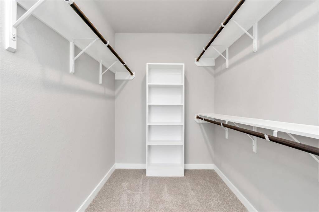 Experience luxury in this spacious walk-in closet with high ceilings and plush carpet. Warm paint tones, built-in shelving, and dark finishes create a contemporary and functional retreat. Sample photo of completed home with similar floor plan. As-built interior colors and selections may vary.