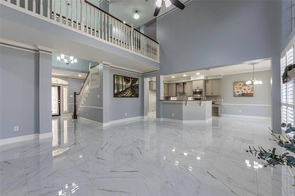This is a spacious, open-concept living area with stacked stone gas log fireplace, high ceilings, large windows allowing for plenty of natural light, and a seamless transition to the kitchen. The space features polished flooring and a comfortable seating area.