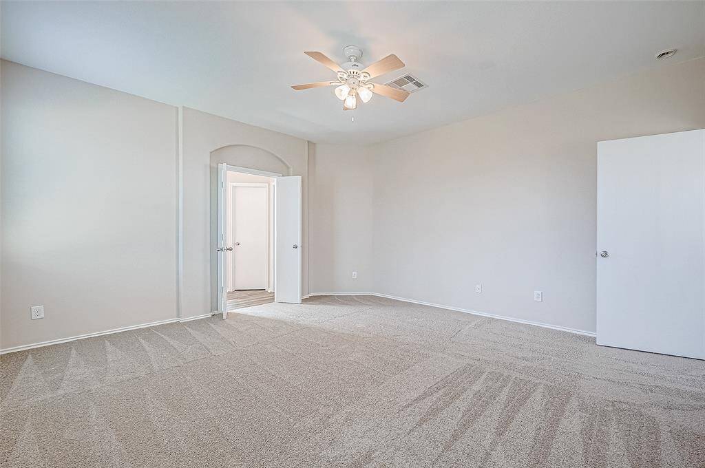 This spacious primary bedroom offers a serene retreat with soft neutral tones and plush new carpeting. The elegant ceiling fan enhances comfort, while the arched doorway leads to a private en-suite, creating a luxurious yet cozy ambiance.