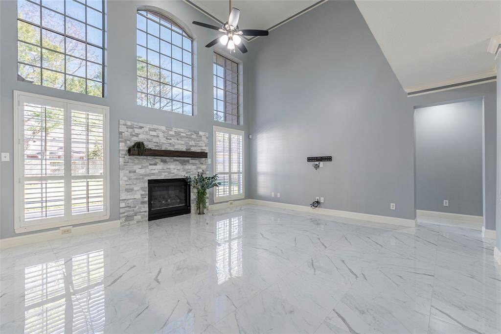 The room is well-lit, with a two-story ceiling, and has an elegant staircase leading to the upper level. Floor to ceiling windows with stacked stone fireplace, plantation shutters and beautiful backyard views.