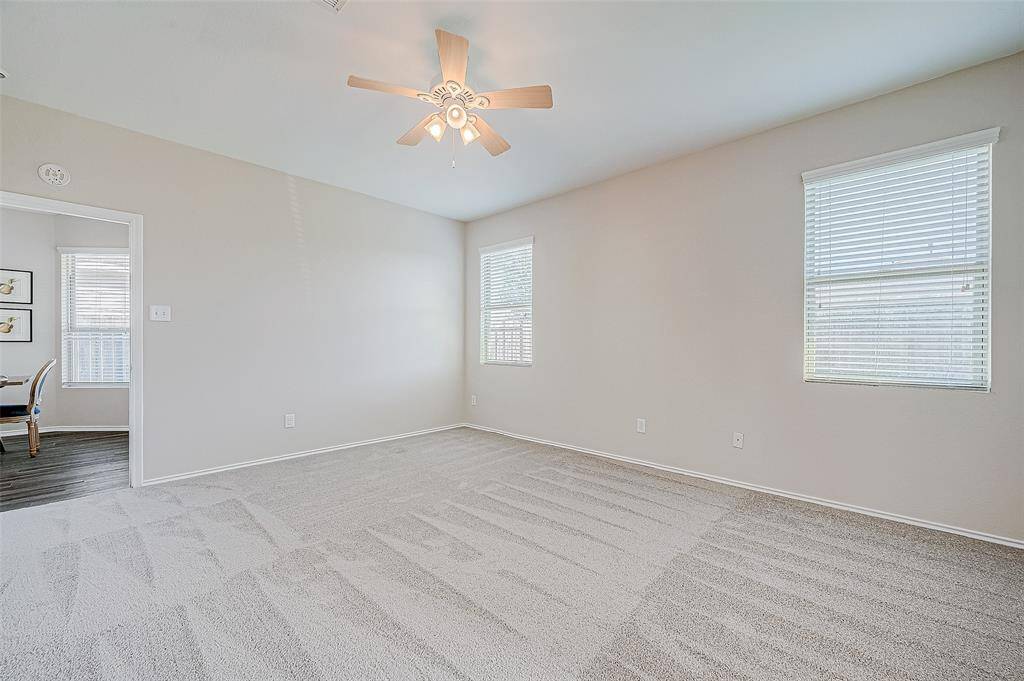 This bright and spacious bedroom offers soft carpet flooring and ample natural light streaming through the dual windows. A ceiling fan adds a touch of functionality and comfort, while the neutral wall tones provide a perfect canvas for personalization. The open doorway offers a glimpse of the connected living space for easy access.