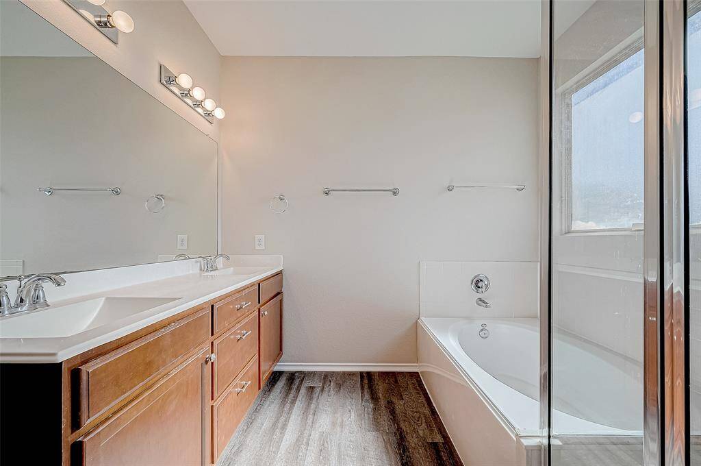 This primary ensuite bathroom showcases a luxurious double-sink vanity with rich wood cabinetry and polished chrome fixtures. The large mirror and elegant lighting elevate the space, while the inviting soaking tub and separate shower provide both relaxation and convenience. A perfect blend of style and functionality!