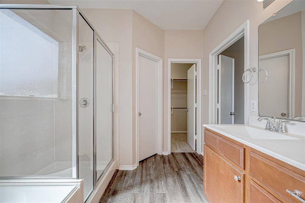 This bathroom offers a practical layout featuring a sleek glass-enclosed shower and a modern vanity with clean lines and ample counter space. The doorways lead to a spacious walk-in closet and an exit to the adjacent room, ensuring convenience and functionality. The neutral tones and durable BRAND-NEW vinyl plank flooring complete the polished look of this private retreat.