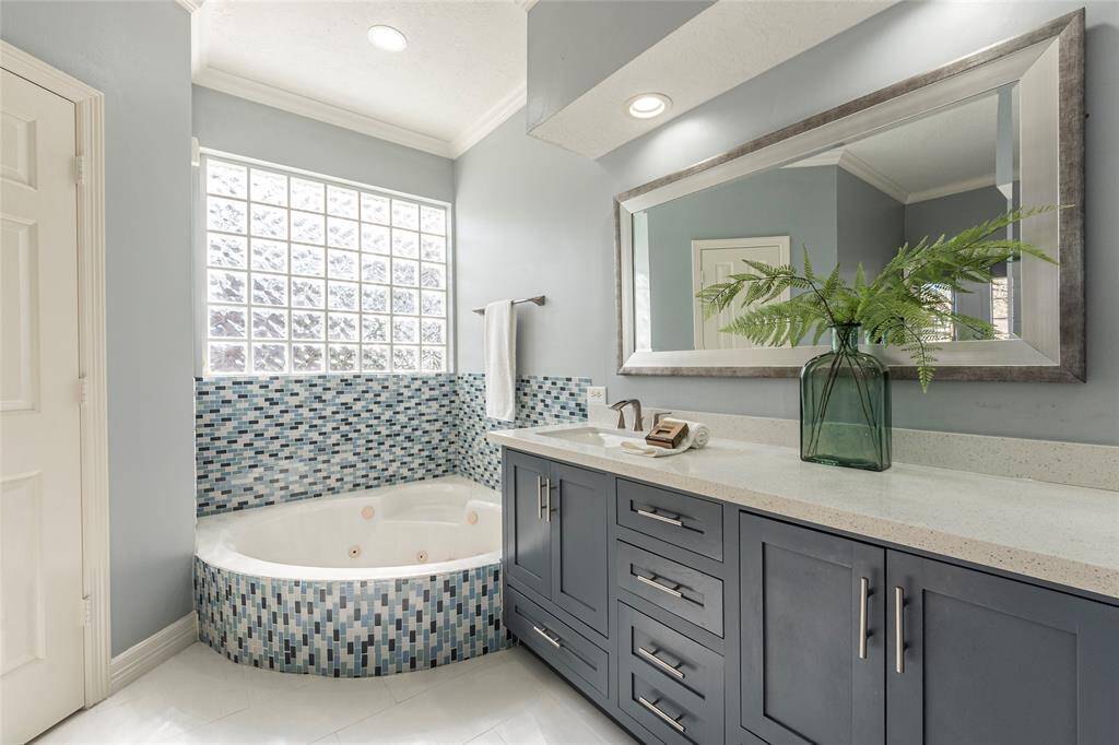 One of two vanity areas in the primary bath with large jetted tub and tile backsplash.