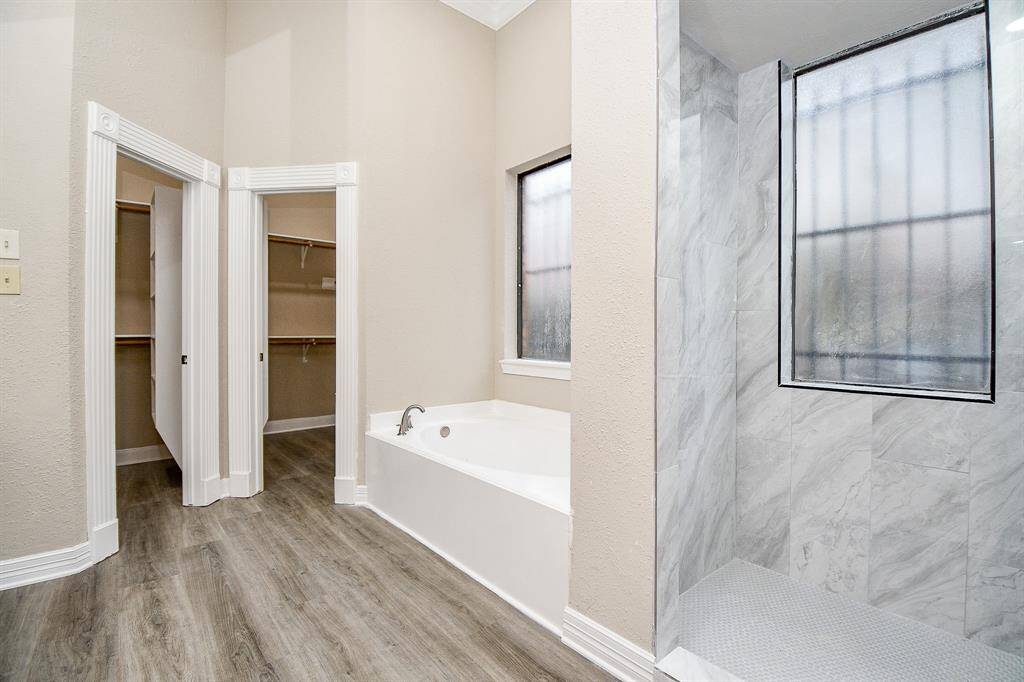 This well-appointed ensuite bathroom proudly belongs to the bedroom that is tucked away from the gameroom.  It offers a fun & luxurious retreat. The vanity boasts dual sinks with ample countertop space, while the separate tub and shower provide options for relaxation. Large mirrors reflect natural light, creating an airy and spacious feel.