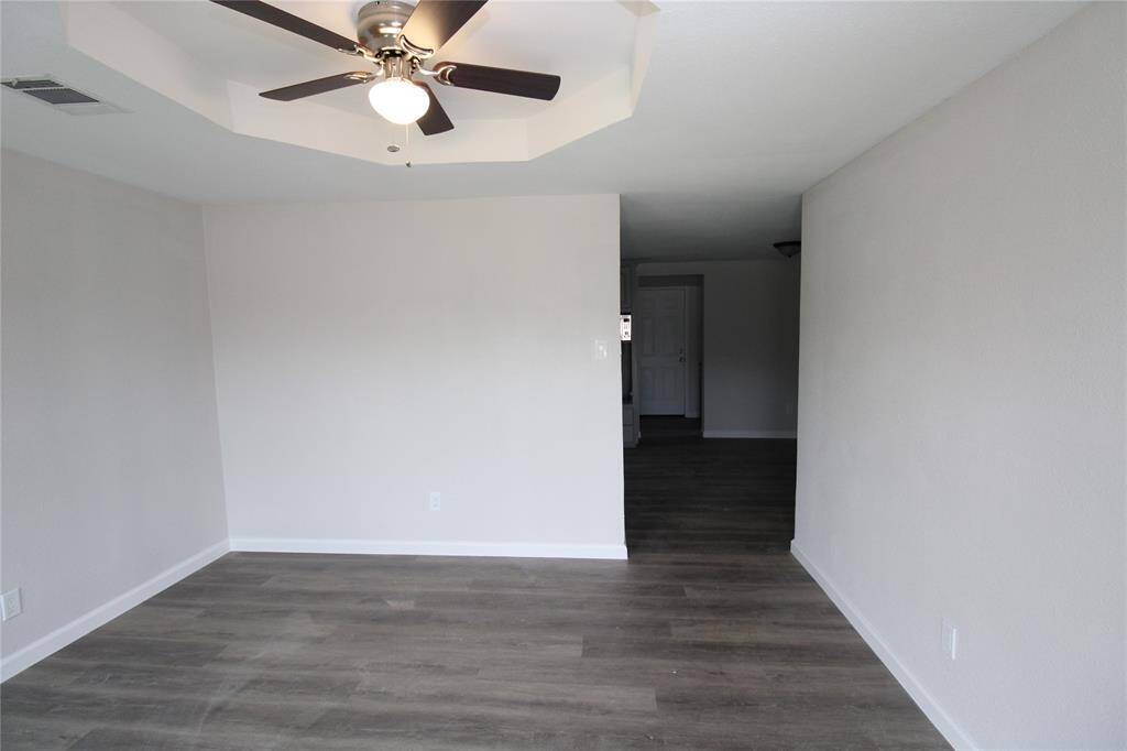 This room features neutral walls and plank flooring, with a ceiling fan and light fixture. It's an open, versatile space.