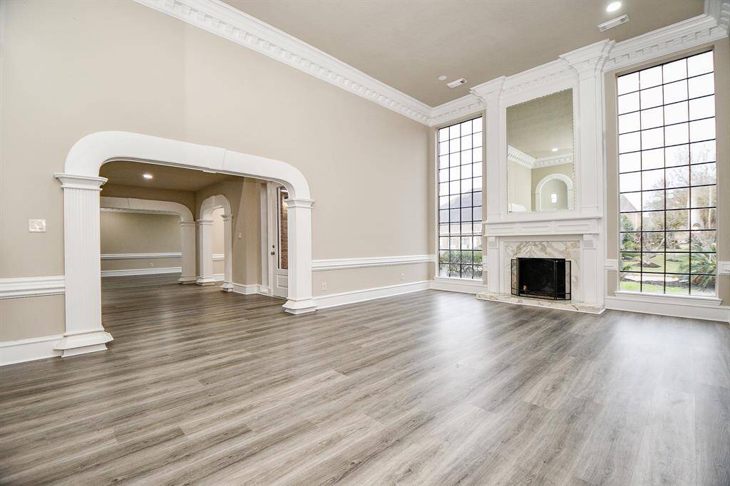 This elegant formal living room boasts floor-to-ceiling windows on either side of the fireplace, creating a bright and airy atmosphere. Recessed lighting and tall ceilings enhance the spacious feel of this inviting space. Opposite the fireplace, a convenient wet bar is perfect for entertaining guests!
