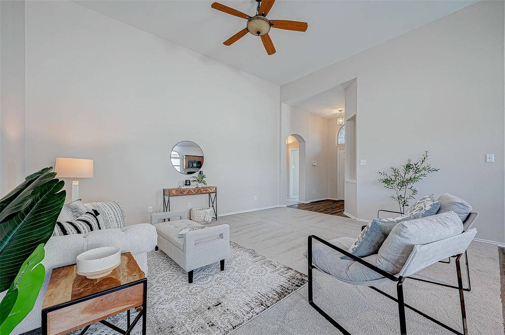 The living room exudes modern elegance with its high ceilings, neutral tones, and a chic ceiling fan. A stylish and cozy area that is perfect for relaxing or entertaining. The open view to the entryway enhances the sense of flow and spaciousness throughout the home.