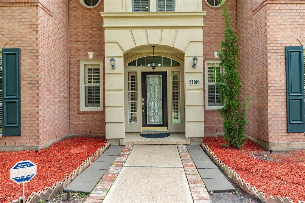 Grand entrance features an arched entry, exterior lighting, stone accent and elegant glass door, complemented by exterior shutters and a neatly landscaped path with fresh mulch.