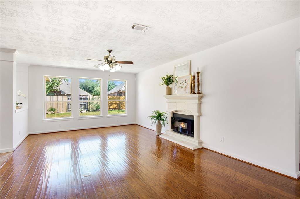 The family room features stunning wood floors that create a cozy yet modern feel, inviting relaxation and togetherness. A wall of windows floods the space with natural light, offering a panoramic view of the outdoors, while the sleek electric fireplace adds warmth and a touch of contemporary style, making it the perfect spot for family gatherings and quiet evenings alike.