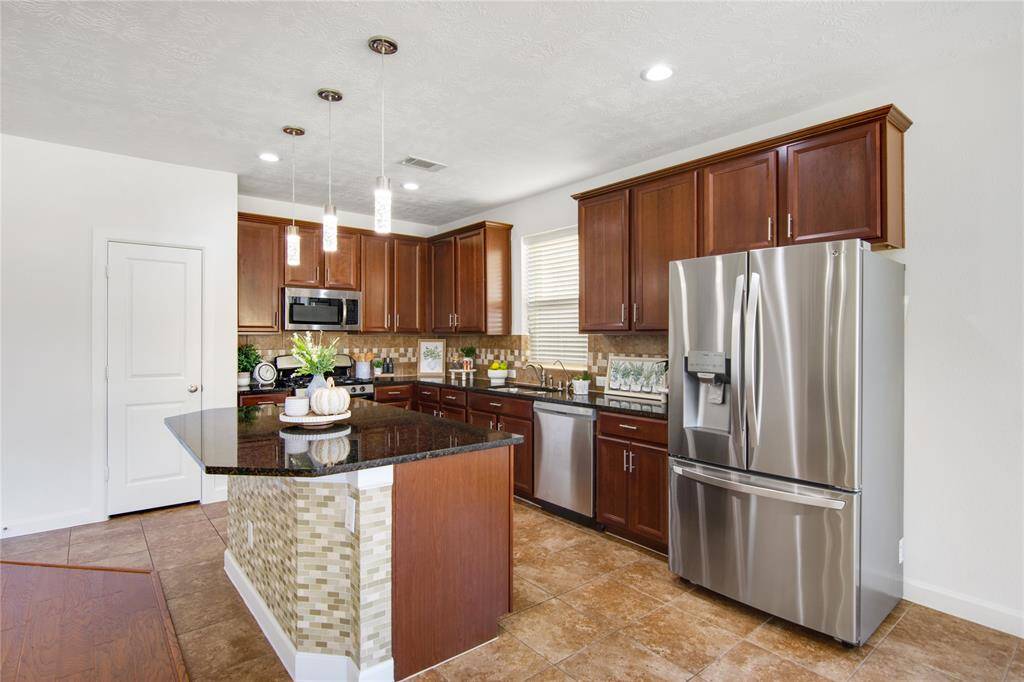 The island showcases beautiful tile work on one side, adding a unique visual element that enhances its overall charm. This thoughtful design detail not only complements the granite countertops but also creates a textured contrast, making the kitchen even more inviting and stylish.