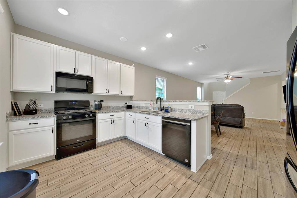 This kitchen features timeless white cabinets, sleek black appliances, and an open layout that overlooks the dining and living areas.