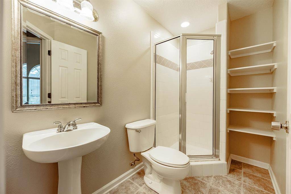 Full bath with corner standing shower and open-shelving for storage needs.