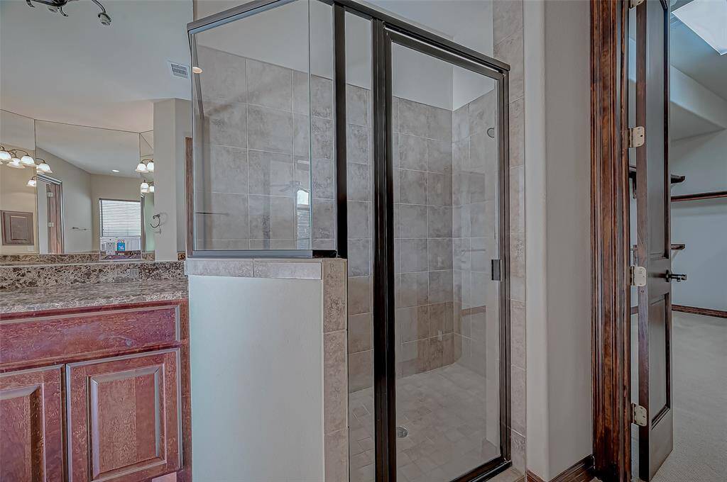 This photo showcases a modern bathroom with a glass-enclosed shower, tile walls, and a granite countertop with wood cabinetry, creating a stylish and functional space.