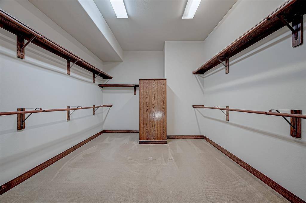 This spacious walk-in closet features ample wooden shelving and hanging rods, ideal for organizing clothing and accessories. The neutral color palette and overhead lighting create a bright and inviting space.