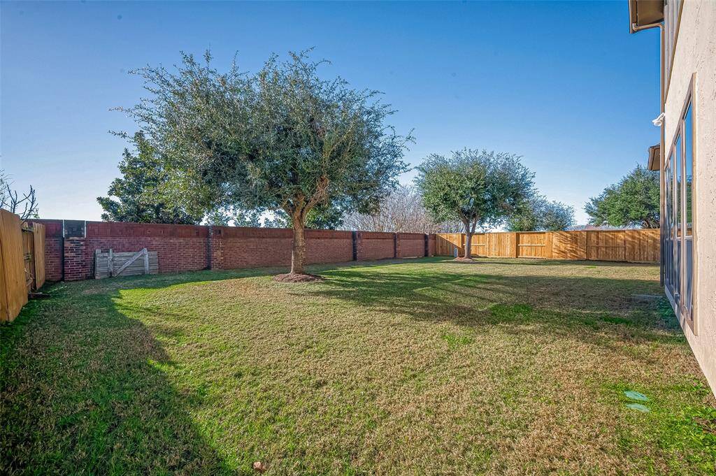 Spacious backyard with a well-maintained lawn, mature trees, and a mix of brick and wooden fencing for privacy. Ideal for outdoor activities and entertaining.
