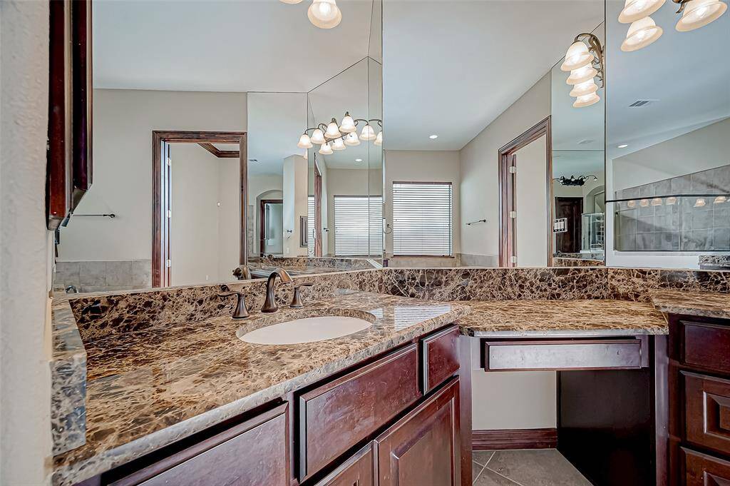 This bathroom features a luxurious design with a marble countertop, dual sinks, and ample mirror space. The dark wood cabinetry adds elegance, and the lighting fixtures provide a warm ambiance.