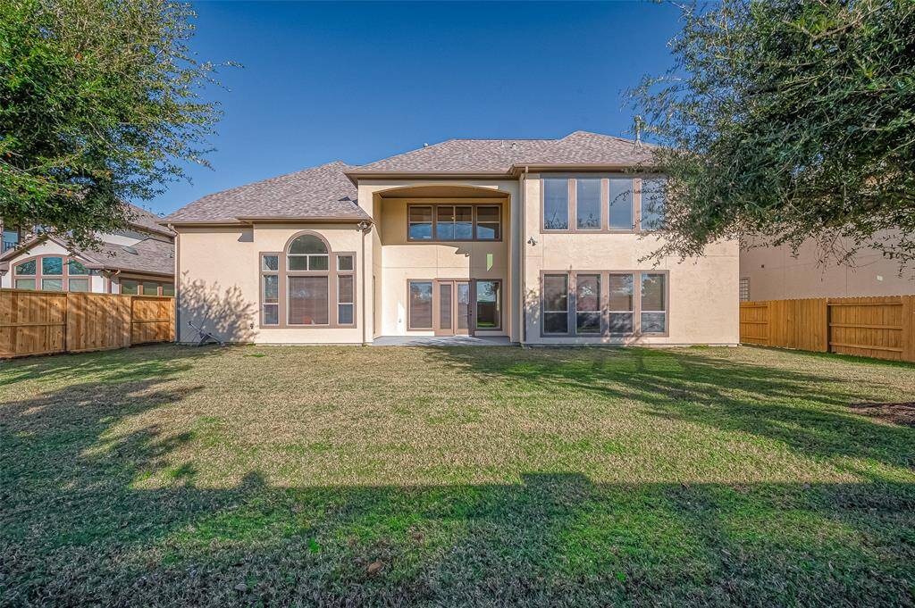 This photo shows a spacious backyard with a large two-story house featuring multiple windows for natural light. The yard is enclosed by wooden fencing, offering privacy and ample outdoor space.