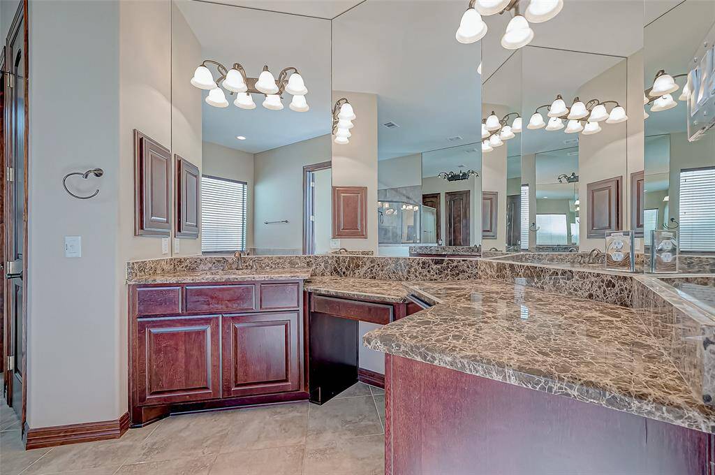 This bathroom features elegant marble countertops, rich wooden cabinetry, and ample lighting. The large mirrors create a spacious feel, while the neutral tile flooring adds a touch of sophistication.
