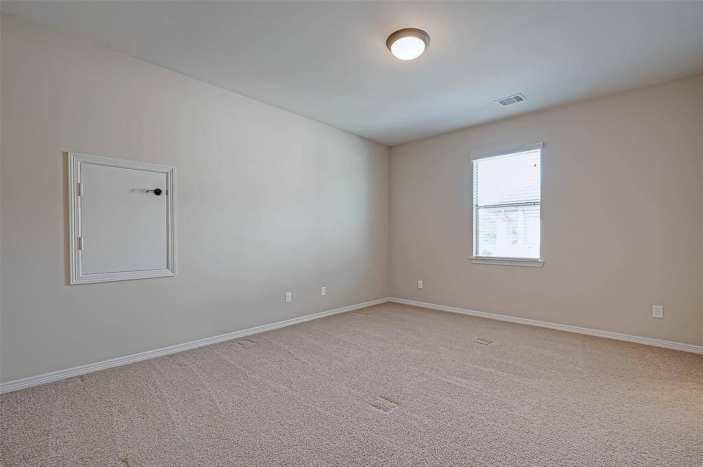 This is a bright, carpeted room with neutral walls, featuring window for natural light and a ceiling light fixture.