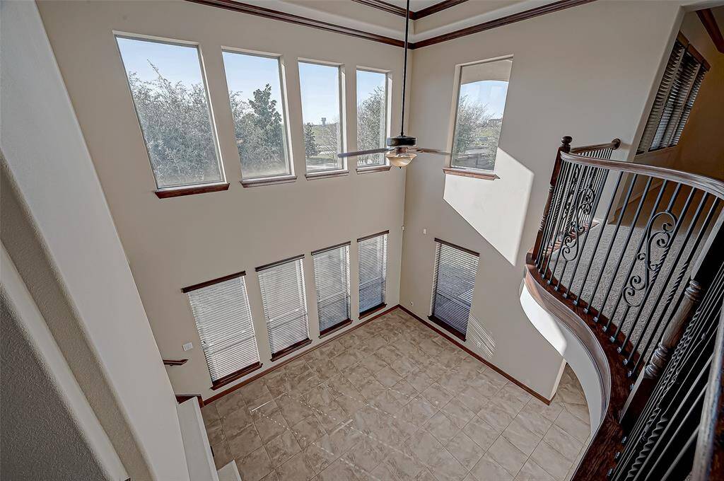 This photo showcases a spacious, two-story living area with large windows that provide abundant natural light. The room features tiled flooring and an elegant wrought iron railing on the upper level, adding a touch of sophistication.