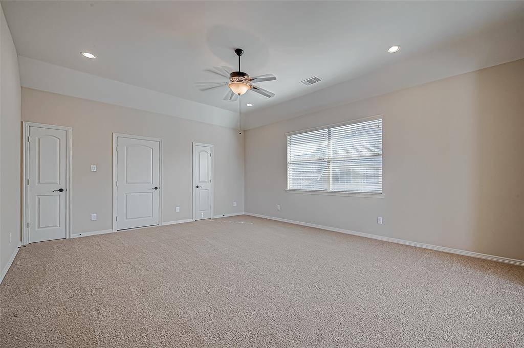 This spacious Gameroom  features neutral carpeting, a ceiling fan, and ample natural light from a large window. It includes multiple doors for closet space or additional access.
