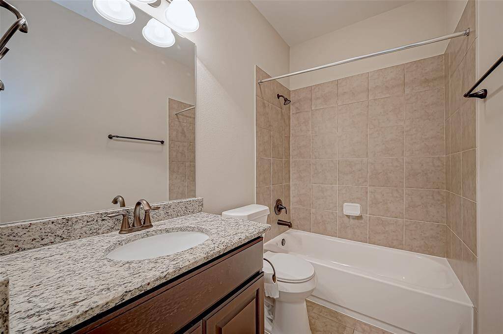 This bathroom features a modern design with a granite countertop, under-mount sink, and bronze fixtures. The shower-tub combo is surrounded by neutral-toned tile, and there's ample lighting above the large mirror.