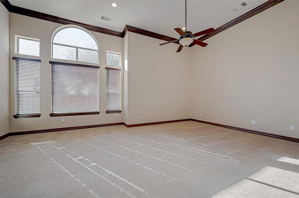 Spacious master bedroom with high ceilings, large arched windows, and abundant natural light. Features a ceiling fan and neutral carpeting, accented by dark wood trim. Perfect for a bright and airy living space.