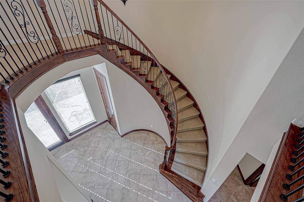 This photo showcases a grand, curved staircase with elegant wrought iron railings and wooden accents, leading down to a tiled foyer with large windows that let in plenty of natural light.