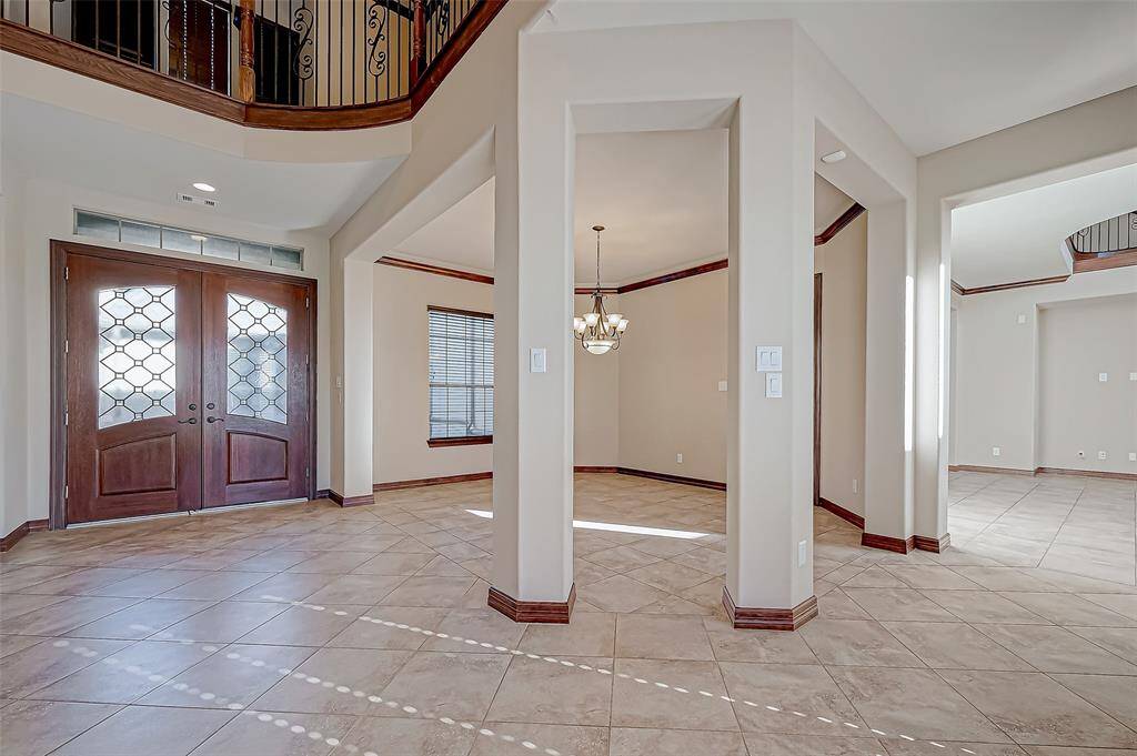 This photo showcases a spacious entryway with elegant double doors and tile flooring. The area features high ceilings, neutral walls, and a stylish chandelier, offering a welcoming and open atmosphere.