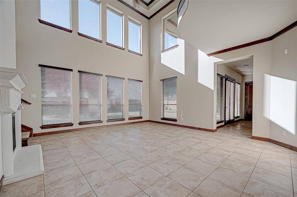 This spacious living area features high ceilings, large windows for ample natural light, and a tiled floor. The open layout is accentuated by a modern staircase and a cozy fireplace, creating an inviting atmosphere.
