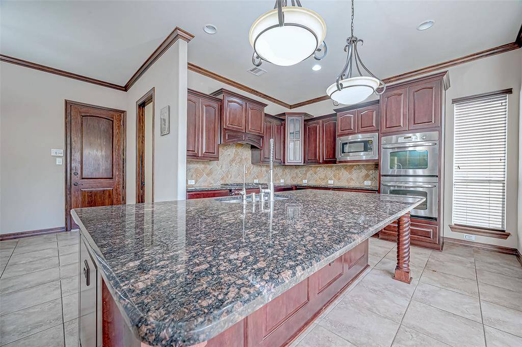 This kitchen features elegant dark wood cabinetry, a large granite island, and modern stainless steel appliances. The open layout is complemented by stylish pendant lighting and a tile backsplash, creating a sophisticated and functional space.