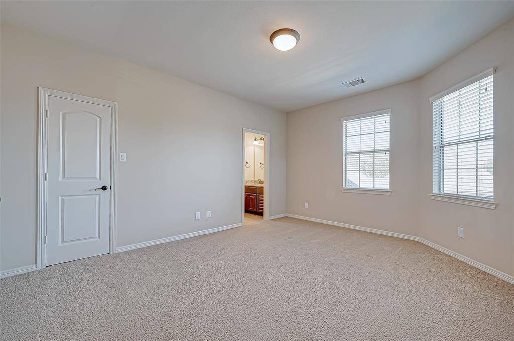 This is a bright, spacious bedroom with carpeted flooring, and two large windows allowing natural light.