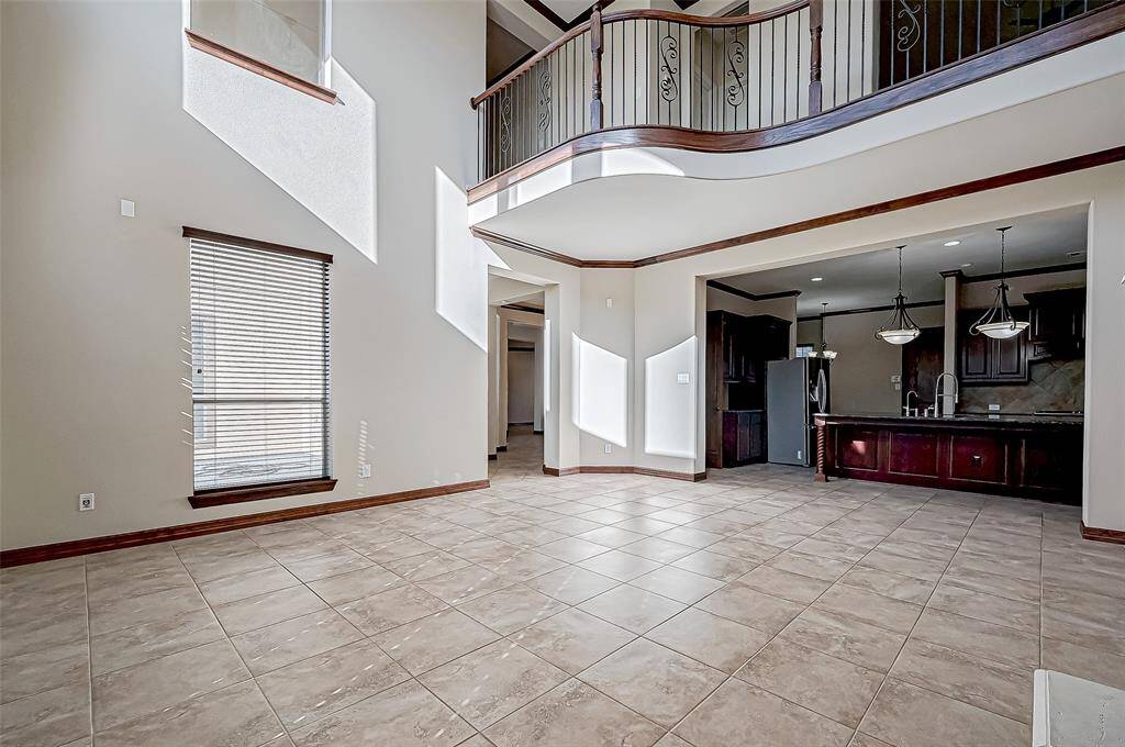 This spacious living area features high ceilings and large windows, allowing plenty of natural light. It has a modern open layout that connects to the contemporary kitchen, which boasts sleek cabinetry and pendant lighting. The tile flooring and elegant railing on the upper level add a touch of sophistication. Perfect for a comfortable and stylish home.