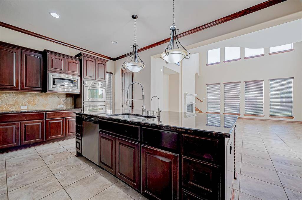 This photo showcases a spacious, modern kitchen with dark wood cabinetry, a central island with a sink, and stainless steel appliances. It opens to a bright living area with large windows and high ceilings, creating an inviting, open-plan space ideal for entertaining.
