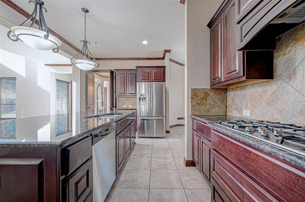 This spacious kitchen features elegant dark wood cabinetry, granite countertops, and a stainless steel refrigerator. It includes a built-in gas cooktop and modern pendant lighting, with large windows providing natural light.
