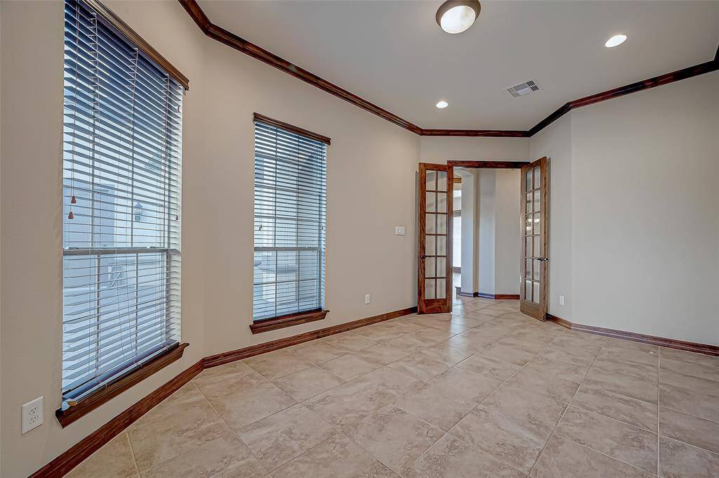 This Office room features large windows with blinds, allowing for ample natural light. It has tiled flooring and elegant wood-trimmed French doors, creating a bright and inviting space.