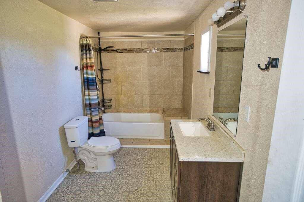 This bathroom features a clean, modern design with neutral tiles, a bathtub-shower combination and a vanity with a large mirror. New vinyl flooring. The space is well-lit with overhead and vanity lighting.